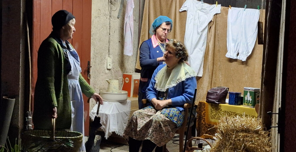 Theaterszene mit Schauspielern in historischen Kostümen vor rustikaler Kulisse mit Strohballen und aufgehängter Wäsche