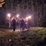 Gruppe mit brennenden Fackeln bei nächtlicher Wanderung durch den Wald in nebligem Ambiente